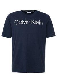 T-paita navy sinisellä värillä, jossa on suuret valkoiset kirjaimet "Calvin Klein" rinnassa.