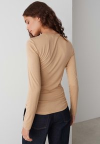 Langademige, getailleerde top in lichtbeige katoenmix, met een ronde halslijn en een gladde textuur, gecombineerd met een donkere spijkerbroek.