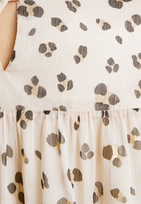 Tissu plissé blanc cassé avec des taches métalliques noires et dorées irrégulières formant un motif léopard sur un vêtement.