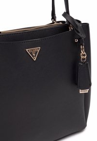 Borsa a tracolla nera in sintetico con logo triangolare in tonalità oro, chiusura con zip e charm rimovibile. Presenta una texture liscia e una forma strutturata.