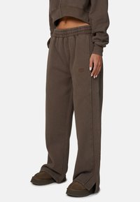 Brązowe bawełniane spodnie dresowe z elastycznym pasem, bocznymi rozcięciami i małym haftowanym logo na biodrze, charakteryzujące się luźnym krojem.