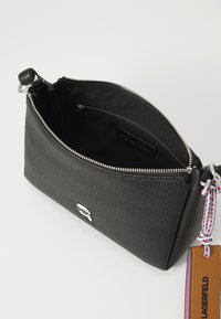 Sac en cuir noir au toucher grainé, avec une fermeture éclair argentée et un détail de porte-clés. L'intérieur est doublé de tissu noir avec une poche zippée intérieure.