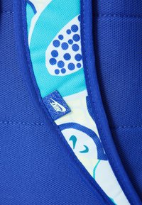 Blå tekstilveske med mønstret interiør i grønn og blå nyanser, prikkete detaljer, og en synlig Nike-logo.