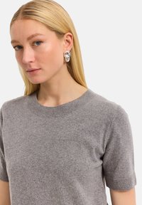 Grauer Kurzarmpullover mit rundem Ausschnitt, aus weichem Material. Besitzt eine glatte Oberfläche und dezente Nähte.