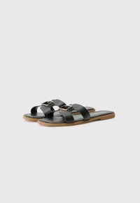 Black flat sandals with three matte straps and a small buckle accent. Flexible rubber sole and a smooth leather insole.