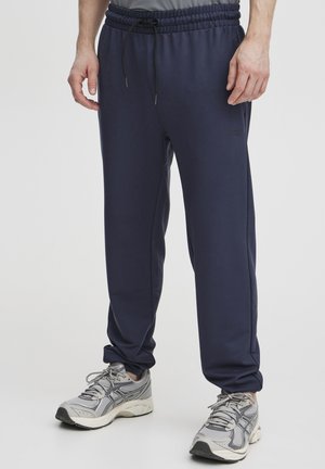 Navy blue jogger pants made of soft fabric, featuring an elastic waistband with a drawstring. Paired with gray athletic shoes.