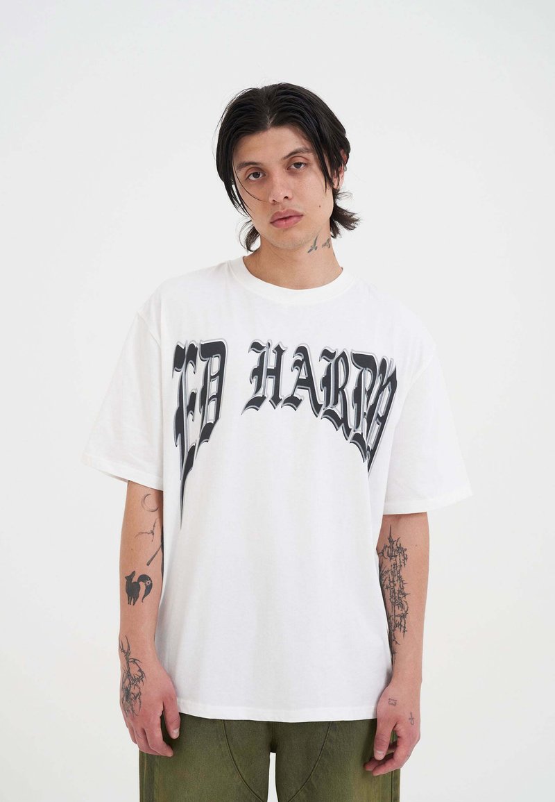 Witte oversized t-shirt met opvallende zwarte letters "ED HARDY" over de voorkant. De stof is glad; de mouwen zijn kort met een ontspannen pasvorm.