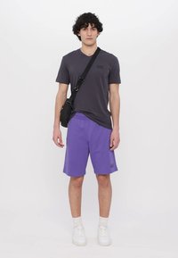 Gray short-sleeve t-shirt, purple athletic shorts, white sneakers, and a black crossbody bag. Simple design with minimal branding.