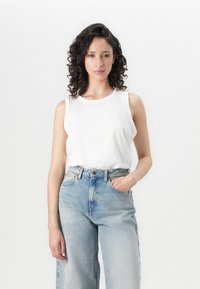 Top sin mangas blanco hecho de una tela suave, combinado con unos vaqueros de cintura alta de color azul claro que tienen un ajuste relajado y un desvanecimiento sutil.