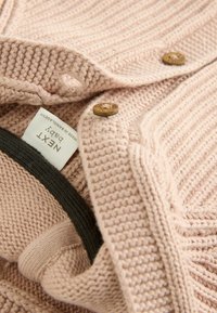 Helle rosa gestrickte Strickjacke mit Holzknöpfen, einem gerippten Textur und einem dunkelgrünen Akzent am Kragen. Etikett innen sichtbar.
