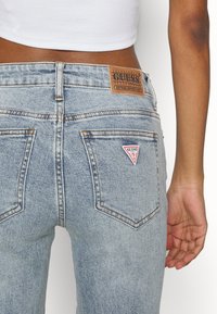 Lichtblauwe denim jeans met een hoge taille, voorzien van een leren merklabel en een driehoekig rood logo op de achterzak.
