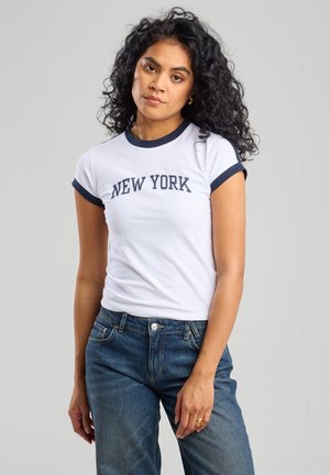 White cotton t-shirt with navy blue ringer sleeves and neckline, featuring "NEW YORK" printed in navy text across the chest. Worn with blue jeans.