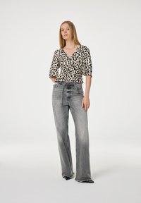 Bloemmotief blouse met een V-hals en korte pofmouwen; gecombineerd met hoge taille, lichtgrijze, wijde jeans met rafelige zoom.