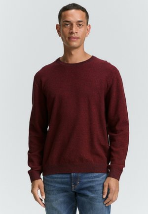 Suéter rojo con textura, de cuello redondo, mangas largas y puños acanalados, combinado con jeans azules.
