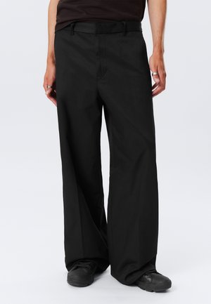 Black wide-leg trousers with a smooth texture and belt loops. Features front pockets and a crease down the front, paired with black shoes.