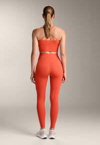 Narancssárga sport crop top vékony pántokkal és hozzá illő, magas derekú leggings. Sima textúra, a hátsó részen diszkrét logóval.
