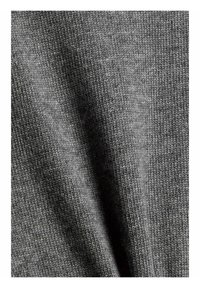 Gros plan d’un tissu tricoté gris côtelé avec une texture visible et une légère ombre, montrant des coutures fines et un motif tissé.