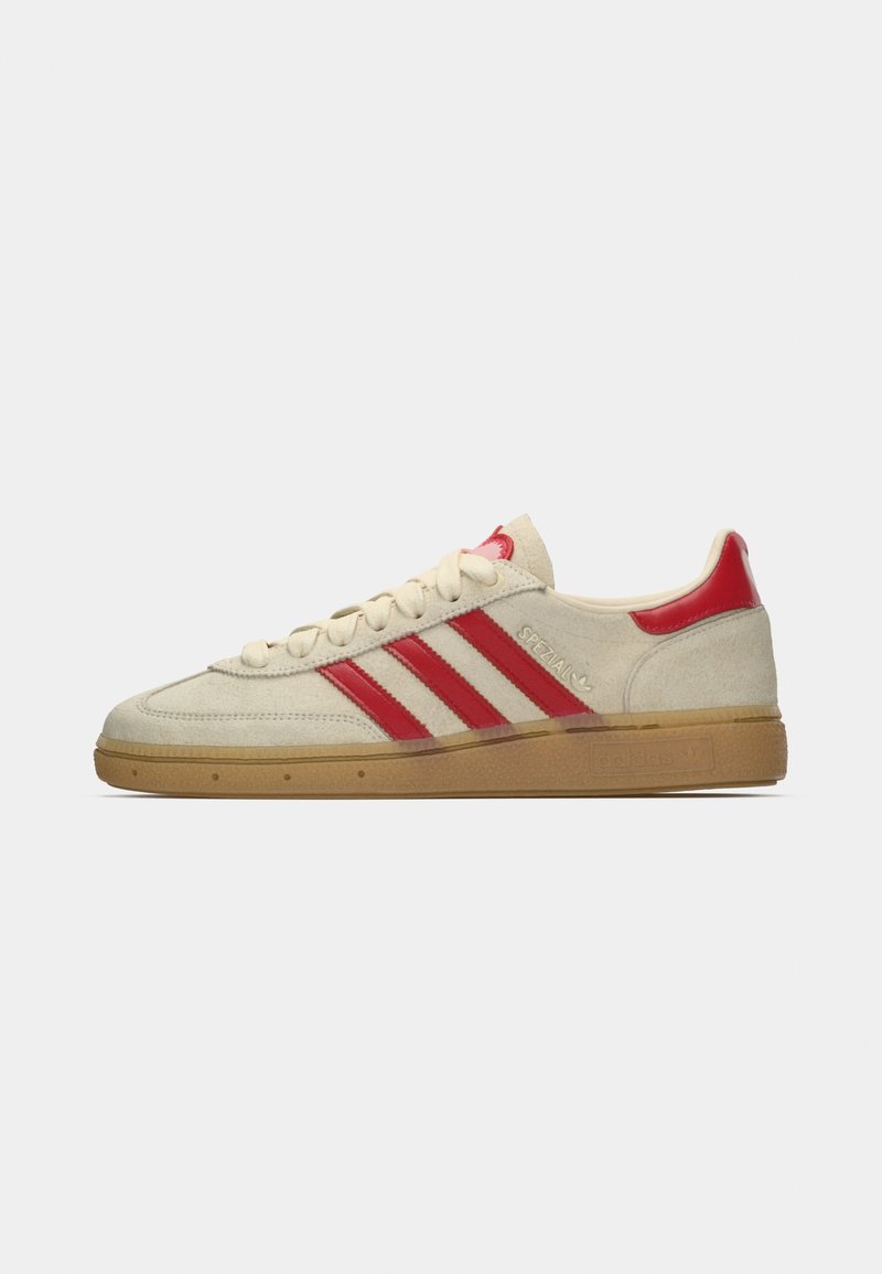 Beige suede sneaker with red stripes and accents, featuring a gum sole and textured upper. Laces in matching color complete the design.