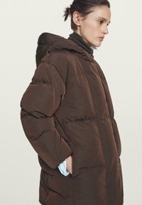 Brown insulated puffer coat with a hood, featuring a zip front, elastic cuffs, and side pockets. Smooth, water-resistant fabric texture.