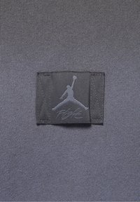 Gros plan sur une étiquette en tissu gris foncé avec un logo Jumpman de basketball cousu et le mot « Flight » en écriture manuscrite en dessous.