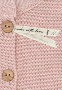 Detail eines rosa gestrickten Pullovers mit Holzknöpfen und einem Stoffetikett, auf dem "mit Liebe gemacht" steht. Glatte Textur und feine Nähte sind sichtbar.