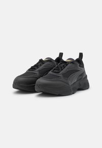 Scarpe sportive nere con tomaia testurizzata, realizzate in materiali mesh e sintetici, suola spessa e una linguetta sul tallone per facilitare l'indossamento.