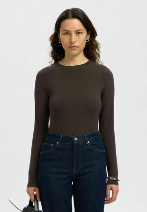 Body à manches longues, ajusté, en brun et fabriqué dans un matériau doux ; associé à un jean en denim foncé taille haute. Design minimaliste et col rond classique.