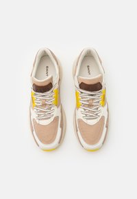 Sneaker mit einer Mischung aus braunen, cremefarbenen und gelben Materialien, mit strukturiertem Stoff, Schnürdesign und prominentem Logo auf der Zunge.