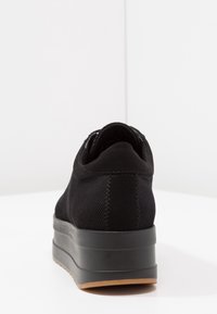 Musta lenkkari, jossa on teksturoitu kangaspäällinen, korotettu pohja ja kontrastivärinen kumipohja. Mallissa on sileä takaosa ja ommellut yksityiskohdat.