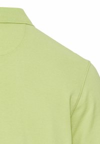Lichtgroen polo-shirt van een gestructureerde stof, met een standaard kraag en korte mouwen. Naaddetails zijn zichtbaar op de schouder.