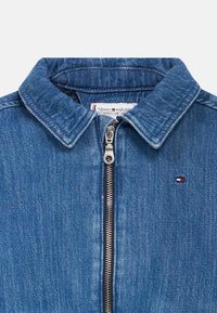 Μπλε τζιν μπουφάν με γιακά, ασημένιο φερμουάρ μπροστά, μικρό λογότυπο Tommy Hilfiger στο στήθος και εμφανής ετικέτα της μάρκας στο εσωτερικό του γιακά.