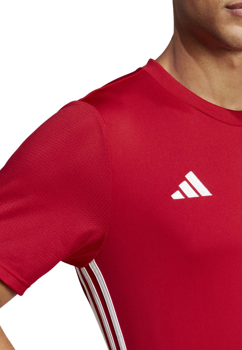 Rode sporttrui van gladde stof met een gestructureerd paneel op de schouder. Voorzien van het witte Adidas-logo en drie witte verticale strepen.