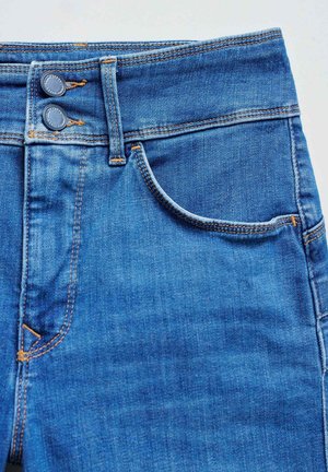 Jean en denim bleu foncé avec une texture lisse, présentant deux boutons ronds en métal à la taille haute et une poche frontale avec des détails de couture.