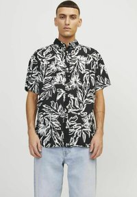 Camisa negra de manga corta con un patrón floral blanco, cuello abotonado y corte relajado. El tejido parece suave con una textura ligera.
