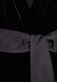 Vêtement en velours noir avec une large ceinture en satin gris nouée en un nœud plat à la taille.