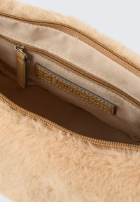 Faux-Fur-Beutel in hellbeige mit Reißverschluss. Das Innere verfügt über ein glattes beiges Futter und ein kleines Fach mit einem Etikett.
