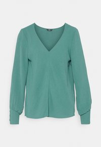 Camisa verde de manga longa com decote em V, elaborada em tecido macio, com mangas ligeiramente franzidas e detalhes em botão nos punhos. Textura suave.