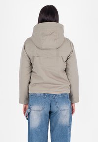 Giacca con cappuccio grigio chiaro dal taglio boxy, caratterizzata da un design con yoke sul retro, abbinata a jeans in denim blu sbiadito con tasca posteriore.