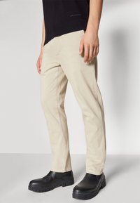 Beige bomulls chinos med slim fit, med sidelommer og taperet ben, kombinert med svarte gummisåler ankelstøvler.