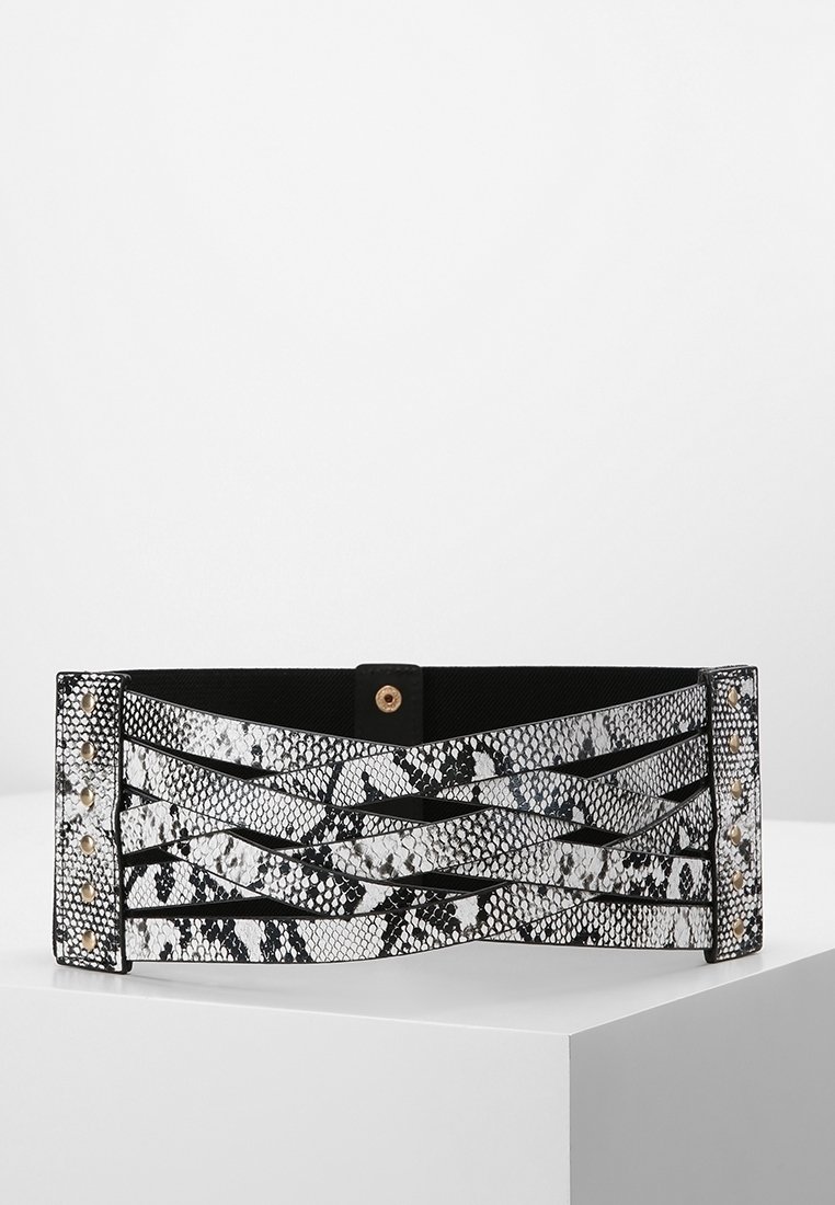 Large ceinture noire et blanche à motif peau de serpent avec des lanières croisées et des clous dorés à chaque extrémité, fermée par un bouton-pression central.