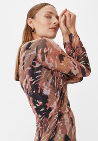 Langärmliges Mesh-Kleid mit einem abstrakten Blumenmuster in Brauntönen, Rosa und Schwarz. Strukturierter Stoff mit Raffung Details an der Taille.