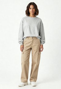 Felpa grigia con spalle scese, abbinata a pantaloni cargo beige con tasche laterali. Scarpe bianche completano l'outfit.