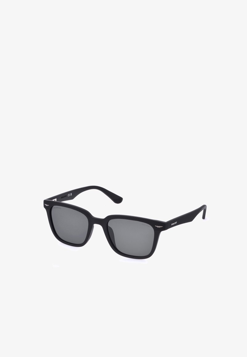 Lunettes de soleil carrées noires avec verres teintés foncés et monture fine texturée, avec petit logo métallique sur les branches.