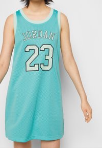 Person som bär en ärmlös turkos mesh-klänning med "JORDAN" och nummer "23" i vit konturerad svart text på framsidan.