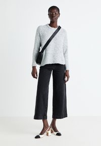 Pull gris éponge à col rond, associé à un jean noir à jambes larges. Complété par des chaussures à talons blocs bicolores noir et blanc.