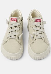 Sneakers beige in tela con punta rotonda, superficie testurizzata, lacci regolabili e logo rosso "CAMPER" sulla linguetta. Suole in gomma con scanalature.