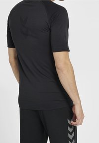 Czarna sportowa koszulka z krótkim rękawem o prążkowanej fakturze i subtelnym logo z tyłu. Posiada dopasowany krój i płaskie szwy dla większego komfortu.