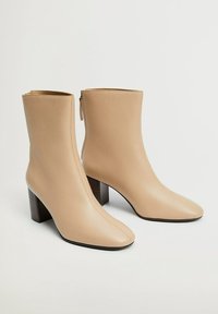 Botas de tobillo de cuero beige con punta afilada y tacón bloque de altura media. Cuentan con una cremallera lateral para ponerse f�ácilmente y una textura suave.