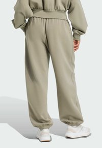 Kaki sweatpants sa suženim fitom, elastičnim pojasom i manžetama. Tkanina je meka, s glatkom teksturom i bočnim džepovima. Uparene su s bijelim tenisicama.