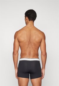 Μαύρο μποξεράκι με λευκό λάστιχο μέσης; σφιχτή εφαρμογή; λεία ύφανση; διαθέτει δύο οριζόντιες ρίγες στο λάστιχο μέσης.